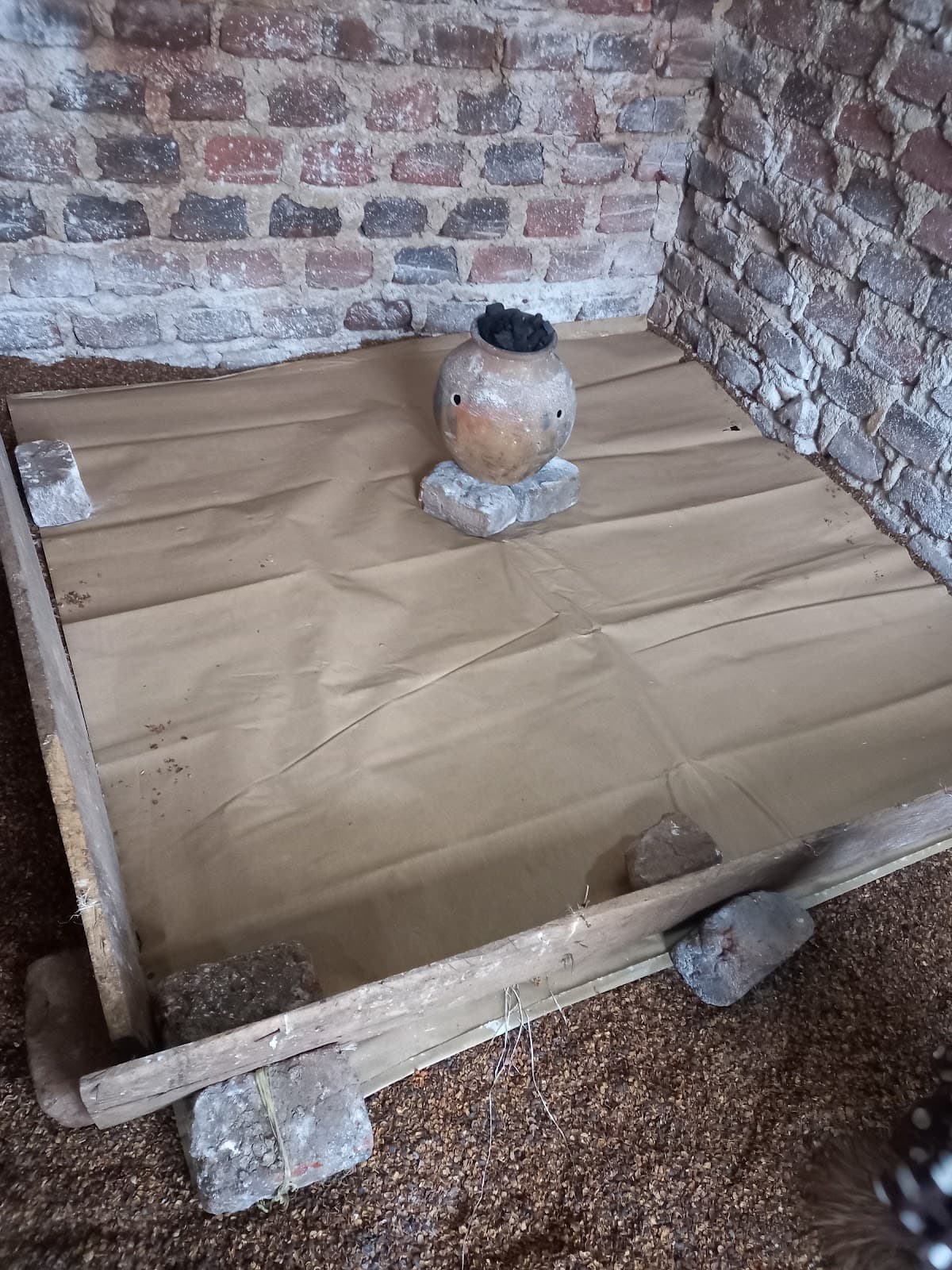 Ein Tontopf mit Holzkohle steht auf Steinen in der Mitte einer Holzplattform.